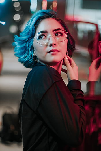 Vibrant portrait of an Asian woman with blue hair and glasses under colorful city lights. HD phone wallpaper