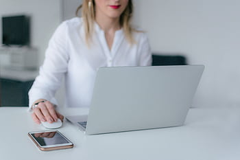 A woman working at a desk using a laptop and smart, exemplifying remote work. HD wallpaper