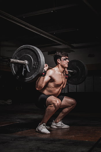Shirtless man performing a barbell squat, showcasing strength and fitness. HD phone wallpaper
