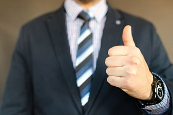 Close-up of a businessman in a suit giving a thumbs up gesture, symbolizing success. HD wallpaper