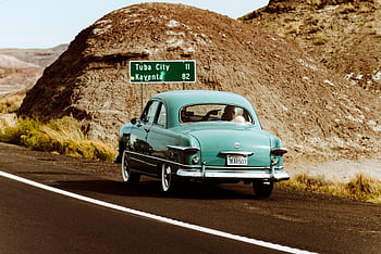 Classic vintage car driving through the scenic desert landscape of Arizona near Tuba City. HD wallpaper