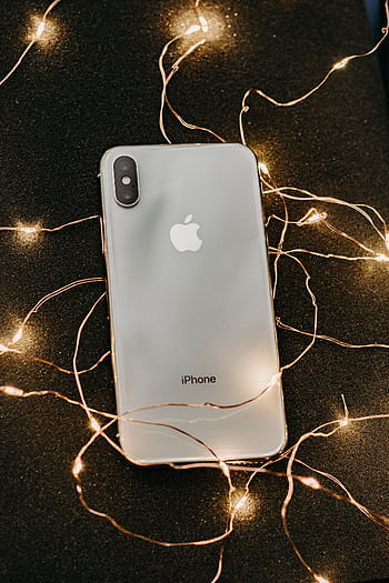 A sleek smart lies on a glittering black surface adorned with warm string lights, showcasing modern technology. HD phone wallpaper