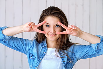 Cheerful woman in denim making a peace sign indoors. Captured in a bright and casual setting. HD wallpaper