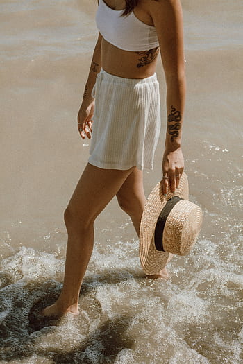 Woman with tattoos and straw hat walking on the beach in summer. HD phone wallpaper