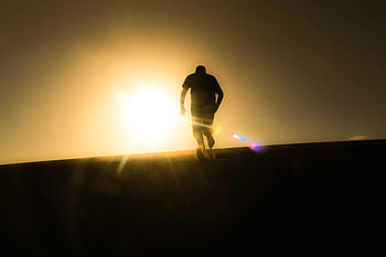 Silhouette of a man running uphill against a bright desert sunrise, capturing a sense of solitude and determination. HD wallpaper