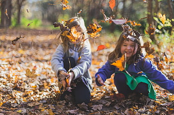Two smiling girls playing joyfully amidst colorful fall leaves in a sunlit forest HD wallpaper