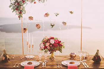 Romantic dining setup with flowers and candles overlooking Santorini waterscape at sunset. HD wallpaper