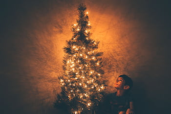 A child smiles at a beautifully lit Christmas tree highlighting the festive glow. HD wallpaper