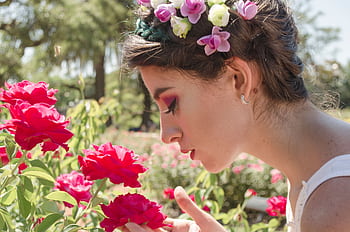 A woman with a floral crown enjoys the fragrant roses in a sunny garden setting. HD wallpaper