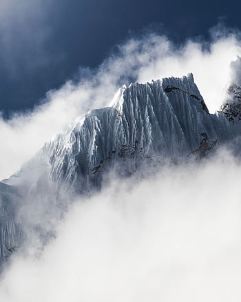 Breathtaking view of a snow-capped mountain peak rising through the misty clouds on a winter day. HD phone wallpaper