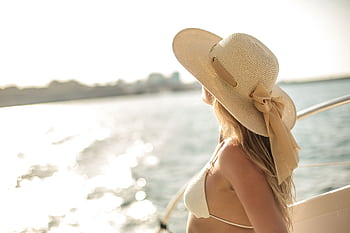 A woman in a straw hat enjoys a sunny day on a yacht, surrounded by tranquil sea views. HD wallpaper