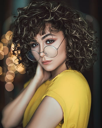Stylish portrait of a woman with curly hair and eyeglasses in a vibrant setting. HD phone wallpaper
