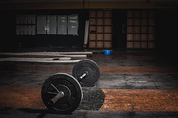 A lone barbell rests in an empty, dimly lit gym, emphasizing strength and solitude. HD wallpaper