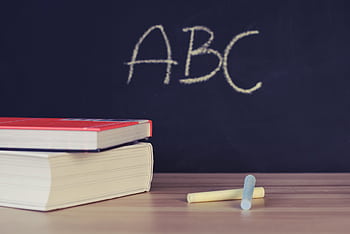 Stack of books and chalk on desk with ABC on blackboard background. HD wallpaper