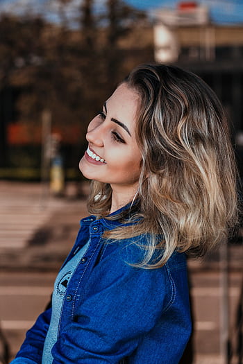 Profile portrait of a young woman smiling while wearing a blue denim jacket outdoors HD phone wallpaper