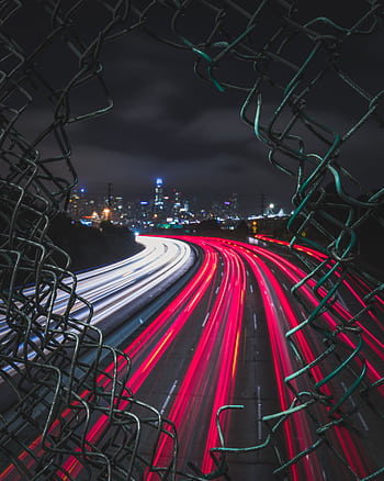 Long exposure captures urban expressway lights through a broken fence at night in San Francisco. HD phone wallpaper