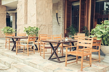 Elegant outdoor café area with wooden chairs and tables, decorated with lush greenery. HD wallpaper