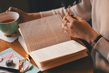 A woman writes in a journal while enjoying a cup of coffee at a wooden table. HD wallpaper