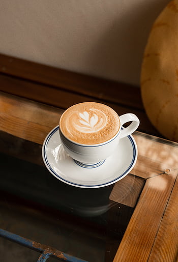 A beautifully crafted cup of coffee with latte art sits on a wooden table, offering a warm ambiance. HD phone wallpaper
