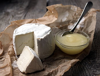 Close-up of gourmet soft cheese with a portion cut out, served with honey on rustic brown paper. HD wallpaper