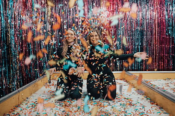 Two women enjoying a vibrant indoor celebration with colorful confetti. HD wallpaper