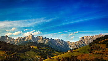A breathtaking landscape of rocky mountains and lush valleys under a vivid blue sky. HD wallpaper