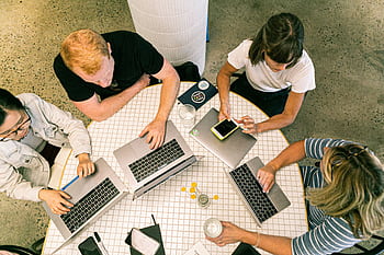 Top view of team collaborating in a modern office around laptops, discussing ideas. HD wallpaper