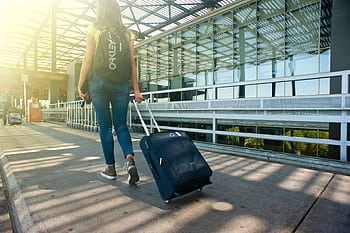 A woman walks with a suitcase outside an airport terminal, ready for travel. HD wallpaper