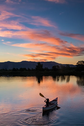 A lone canoeist paddles peacefully on a serene lake during a vibrant sunset. HD phone wallpaper