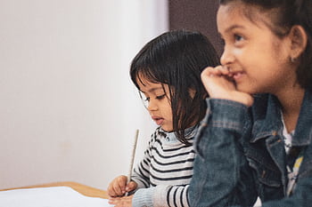 Two young girls joyfully engaged in creative learning indoors, capturing a candid moment of togetherness. HD wallpaper