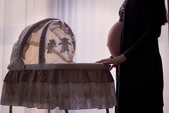 Silhouette of a pregnant woman next to a baby cradle in a softly lit room. HD wallpaper