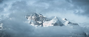 A serene view of snow-capped mountains surrounded by drifting clouds, offering a tranquil winter landscape. HD wallpaper