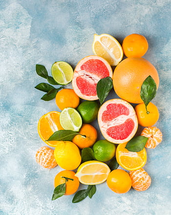 Colorful assortment of fresh citrus fruits including grapefruits and lemons on a vibrant blue background. HD phone wallpaper