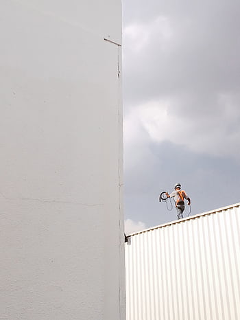 A construction worker stands on a rooftop against a large white wall, highlighting a minimalist aesthetic. HD phone wallpaper