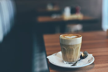 A latte with heart-shaped foam art on a wooden table in a cozy café setting. HD wallpaper