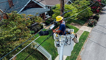 Electrician in a bucket lift repairing power lines from a utility pole in a suburban neighborhood. HD wallpaper