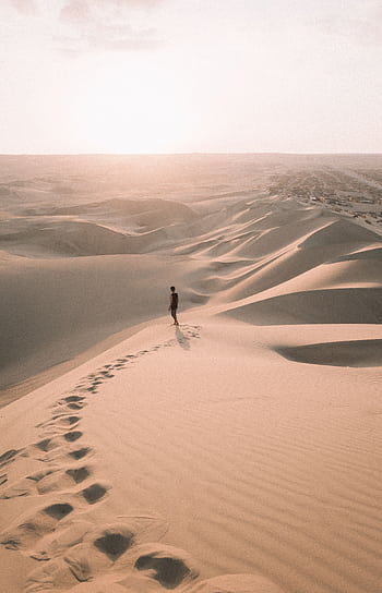 A lone traveler walks across the vast sand dunes of Ica, Peru, under the warm glow of a sunset. HD phone wallpaper