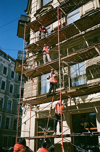 Construction workers on scaffolding renovating a building facade on a sunny day. HD phone wallpaper