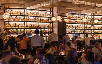 Experience the lively atmosphere of a bustling New York City bar with patrons enjoying nightlife within a stylish indoor setting. HD wallpaper