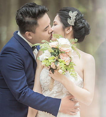 Elegant couple kissing on their wedding day outdoors, holding a floral bouquet. HD phone wallpaper