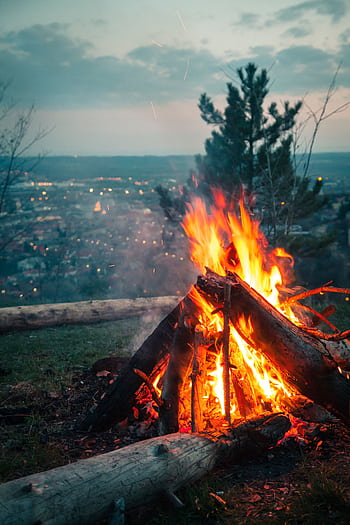 A blazing campfire on a hillside with a city view, evoking warmth and adventure. HD phone wallpaper