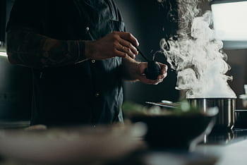 A chef carefully prepares a steamy dish in a professional kitchen setting. HD wallpaper