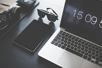 A flat lay of a modern workspace featuring a laptop, tablet, camera, and sunglasses. HD wallpaper
