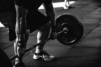 A powerful black and white of a man deadlifting in a gym, showcasing strength and fitness. HD wallpaper