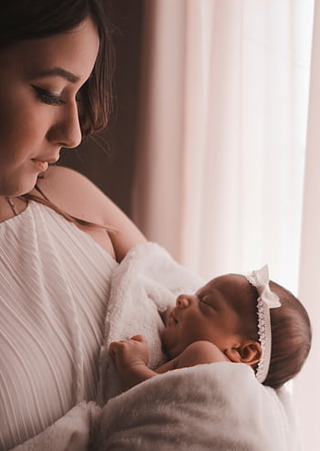 Tender moment of a mother holding her newborn child by a window, capturing love and warmth. HD phone wallpaper