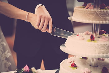 Bride and groom cutting a tiered wedding cake adorned with floral decorations, symbolizing celebration. HD wallpaper
