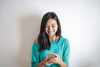 A happy woman in a green top smiling while using her smart indoors. HD wallpaper