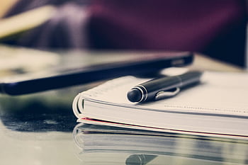 Close-up of an elegant pen resting on an open notebook in a stylish office environment. HD wallpaper