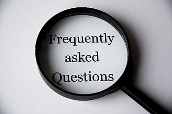 Close-up of a magnifying glass focusing on the phrase 'Frequently Asked Questions'. HD wallpaper