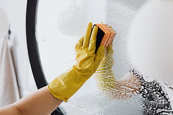 Close-up of a gloved hand cleaning a mirror with a sponge and soap, indoors. HD wallpaper